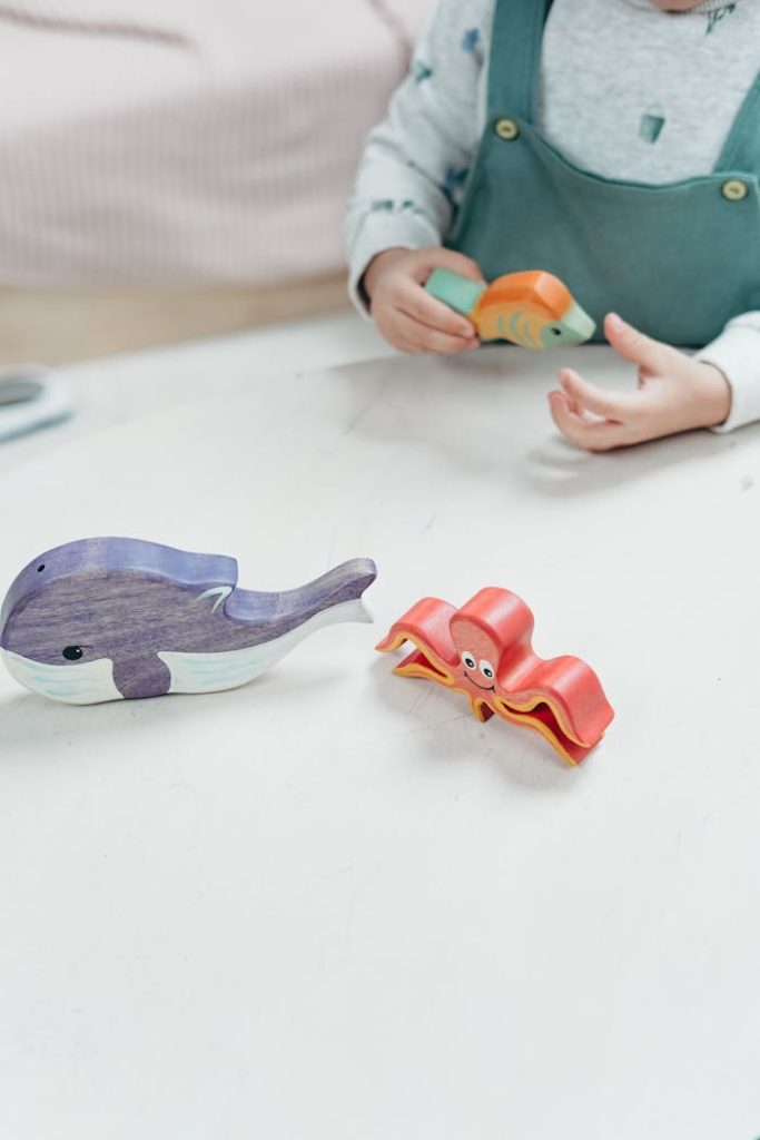 A child engages with vibrant wooden toy animals on a playroom table, highlighting creativity and fun.